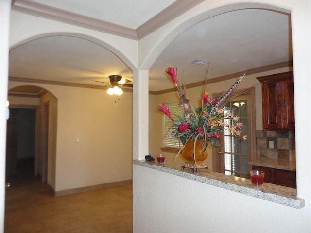 kitchen with baseboards, decorative backsplash, arched walkways, ceiling fan, and ornamental molding