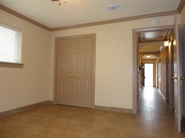 hallway featuring arched walkways, crown molding, visible vents, light tile patterned flooring, and baseboards