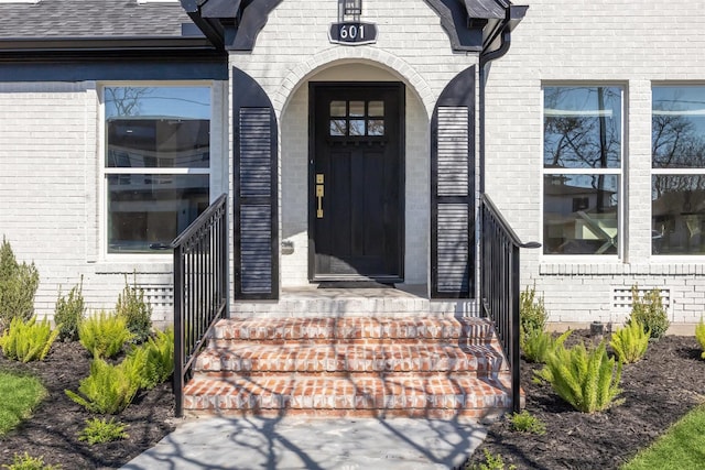 entrance to property featuring brick siding and roof with shingles