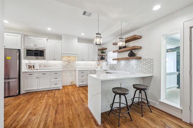 kitchen with open shelves, a peninsula, stainless steel appliances, decorative backsplash, and light wood-type flooring