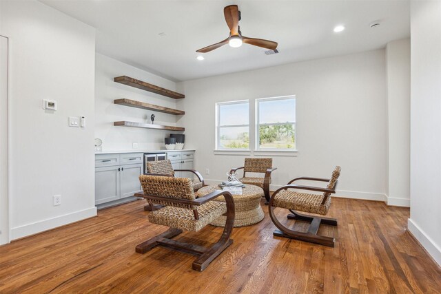 sitting room with visible vents, ceiling fan, baseboards, a dry bar, and wood finished floors