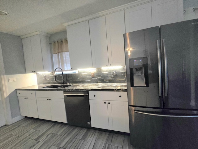 kitchen with black dishwasher, stainless steel fridge, decorative backsplash, white cabinetry, and a sink