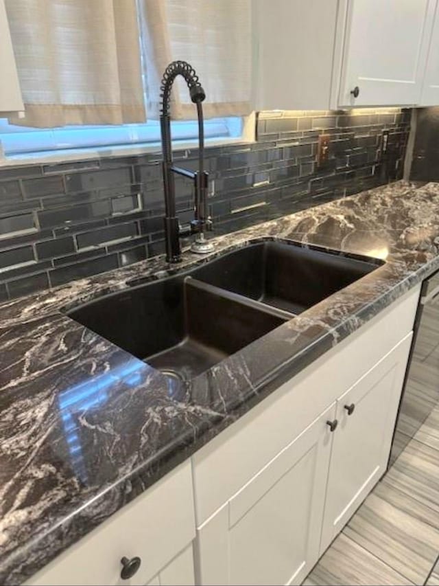 details with tasteful backsplash, dark stone counters, white cabinetry, and a sink