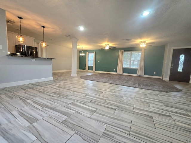 unfurnished living room featuring ornate columns, baseboards, visible vents, and ceiling fan with notable chandelier