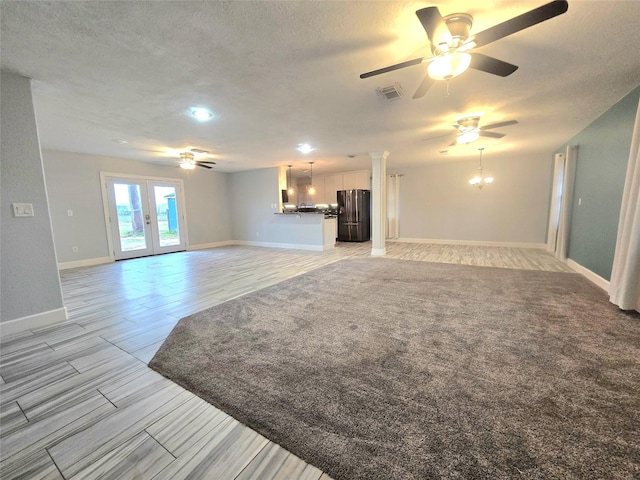 unfurnished living room featuring ceiling fan with notable chandelier, visible vents, a textured ceiling, and french doors