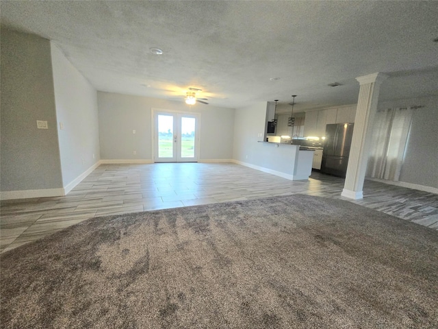 unfurnished living room with a textured ceiling, french doors, baseboards, and light colored carpet