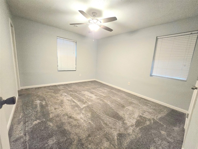 unfurnished room with baseboards, dark carpet, and ceiling fan