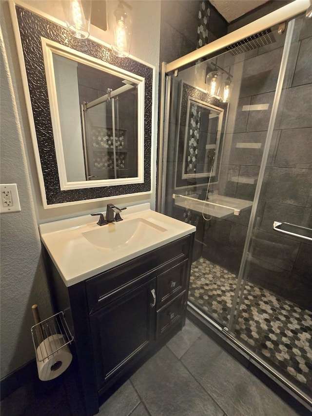 bathroom with a textured wall, tile patterned flooring, a shower stall, and vanity