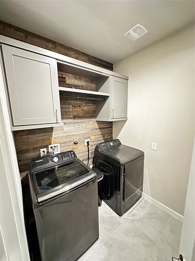 washroom featuring visible vents, cabinet space, wooden walls, washer and dryer, and baseboards