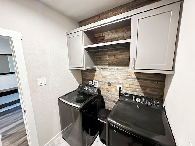 clothes washing area with cabinet space, washing machine and dryer, and wood walls