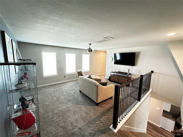 living room with a textured ceiling, dark colored carpet, visible vents, and baseboards