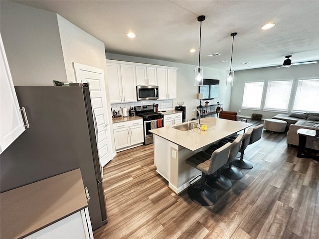 kitchen with light countertops, appliances with stainless steel finishes, a kitchen island with sink, white cabinets, and a sink