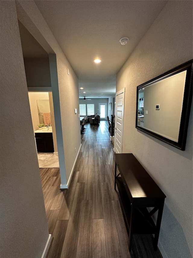 hallway featuring a textured wall, wood finished floors, and baseboards