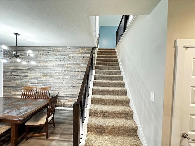 staircase with a textured ceiling, baseboards, and an inviting chandelier