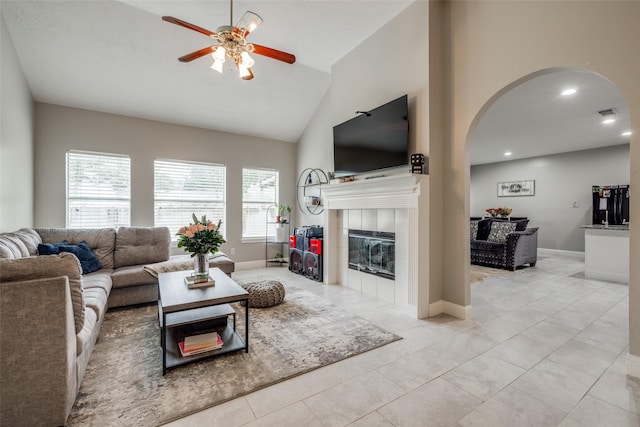 living area featuring baseboards, arched walkways, a ceiling fan, and a tile fireplace