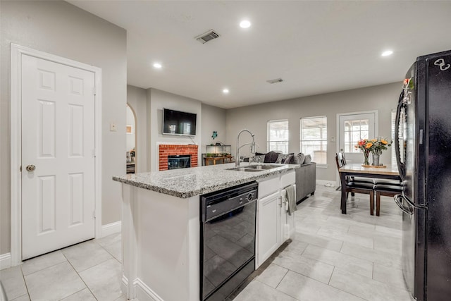 kitchen featuring a sink, visible vents, white cabinets, black appliances, and a center island with sink