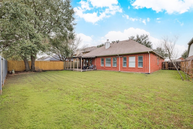 back of property with a fenced backyard, brick siding, a yard, roof with shingles, and a chimney