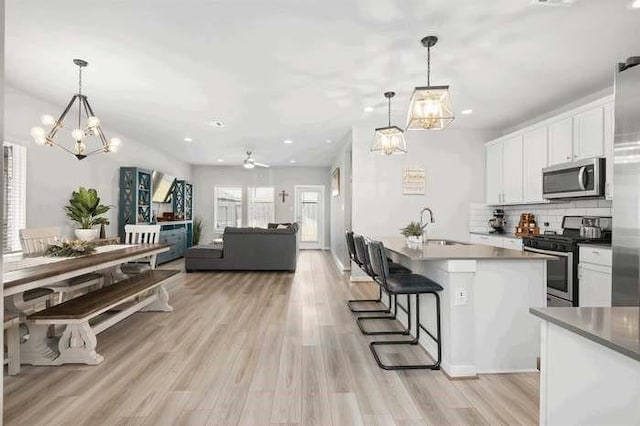 kitchen with a breakfast bar area, white cabinets, open floor plan, appliances with stainless steel finishes, and pendant lighting