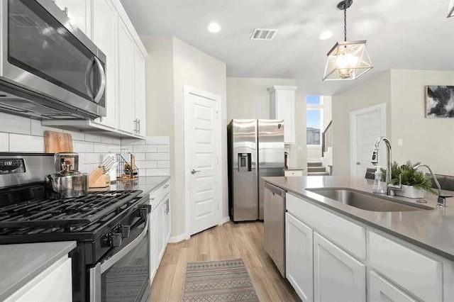 kitchen featuring appliances with stainless steel finishes, pendant lighting, white cabinetry, and a sink