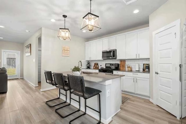 kitchen with decorative light fixtures, stainless steel microwave, white cabinetry, an island with sink, and range