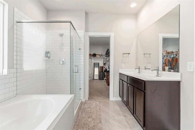 full bathroom featuring tile patterned flooring, a bath, double vanity, a stall shower, and a walk in closet