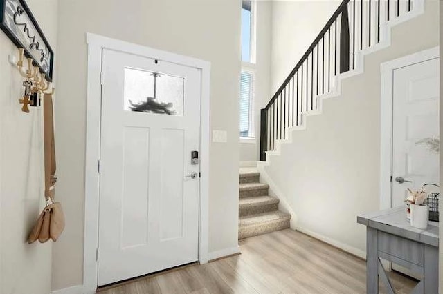 foyer with a high ceiling, light wood finished floors, stairs, and baseboards