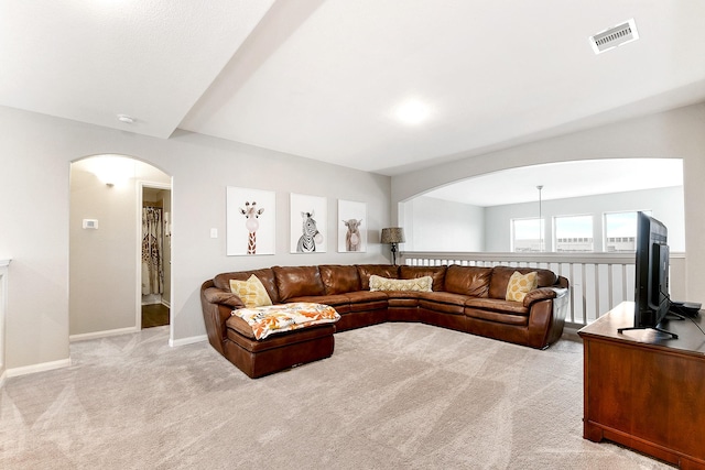 living area with arched walkways, light carpet, visible vents, and baseboards