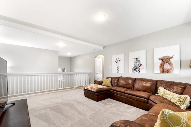 living area featuring arched walkways, beamed ceiling, and light colored carpet