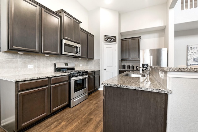 kitchen with appliances with stainless steel finishes, dark wood-style flooring, a sink, dark brown cabinets, and backsplash