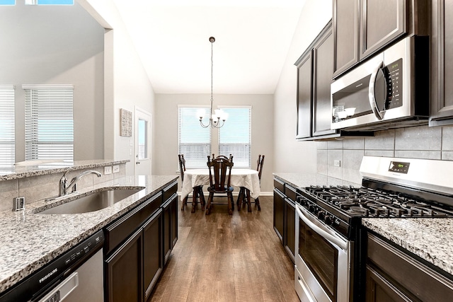 kitchen with dark brown cabinetry, stainless steel appliances, a sink, light stone countertops, and decorative light fixtures