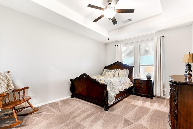 bedroom with a raised ceiling, light colored carpet, visible vents, ceiling fan, and baseboards