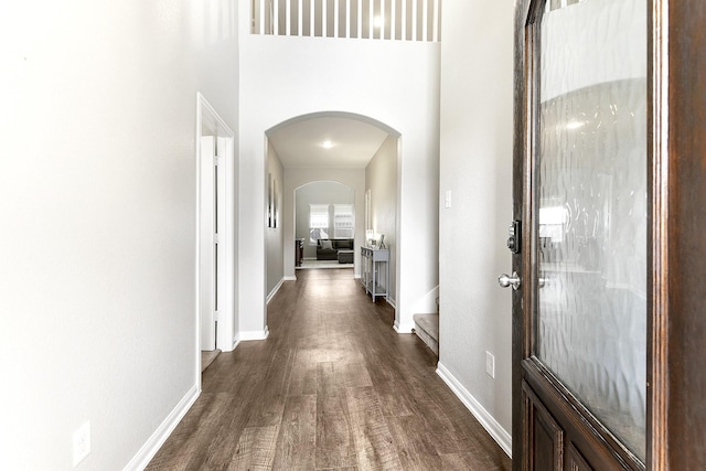 corridor with dark wood-style floors, arched walkways, and baseboards