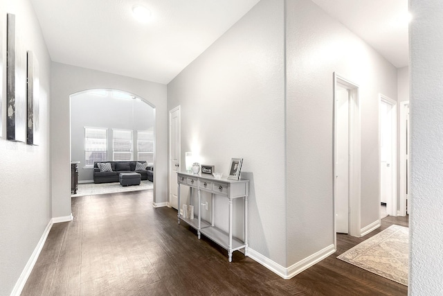 hall with arched walkways, dark wood finished floors, and baseboards