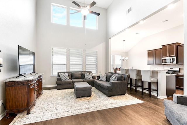 living area featuring visible vents, a high ceiling, wood finished floors, baseboards, and ceiling fan with notable chandelier