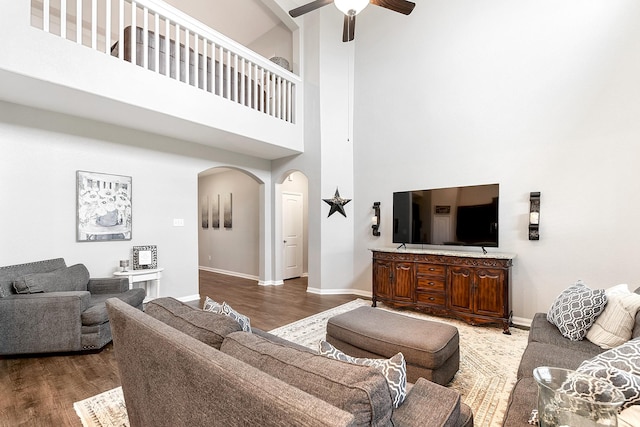 living room featuring arched walkways, ceiling fan, wood finished floors, and baseboards