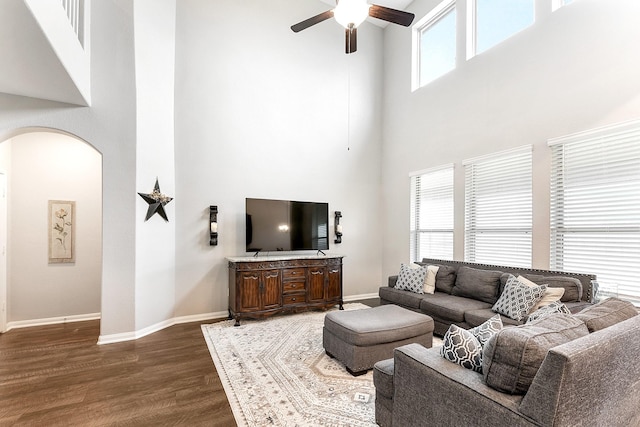 living area with arched walkways, a high ceiling, dark wood-type flooring, a ceiling fan, and baseboards