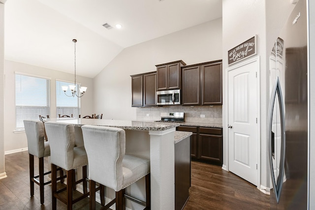 kitchen featuring a center island with sink, hanging light fixtures, light stone countertops, vaulted ceiling, and stainless steel appliances