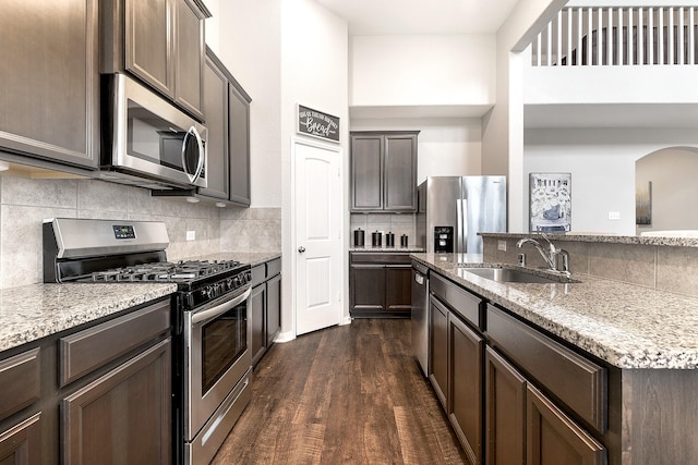 kitchen featuring dark brown cabinetry, a sink, appliances with stainless steel finishes, light stone countertops, and dark wood finished floors