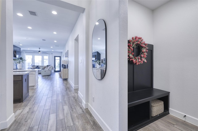 hall featuring visible vents, baseboards, light wood finished floors, and recessed lighting