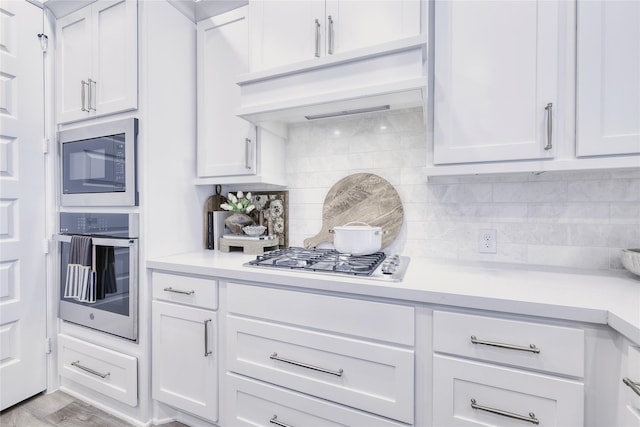 kitchen with appliances with stainless steel finishes, light countertops, backsplash, and under cabinet range hood
