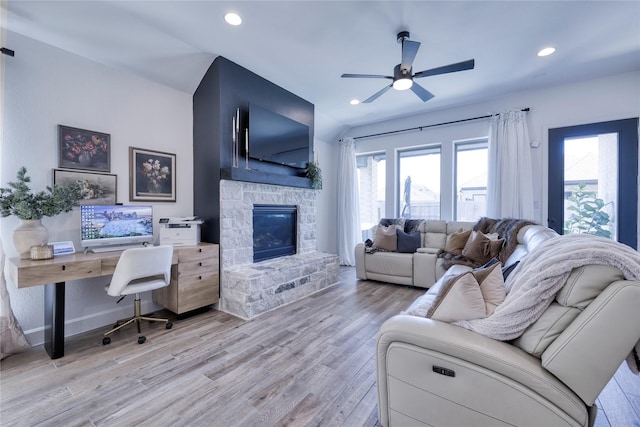 living room with a wealth of natural light, a stone fireplace, light wood-type flooring, and a ceiling fan