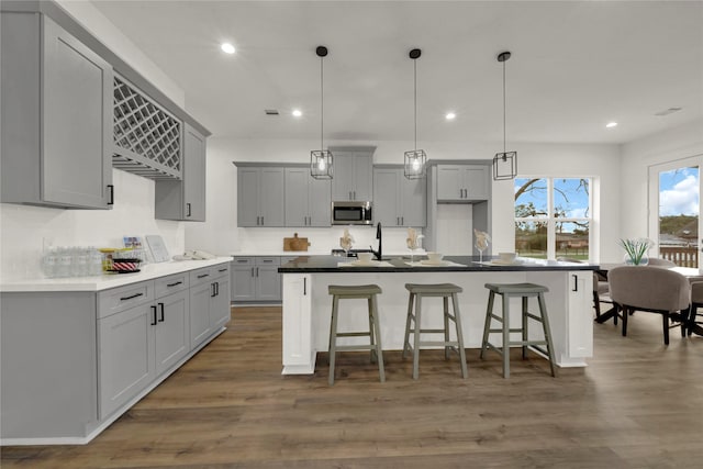 kitchen with wood finished floors, an island with sink, gray cabinets, a kitchen bar, and stainless steel microwave