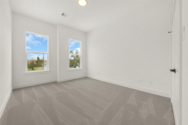 spare room featuring light colored carpet, visible vents, and baseboards