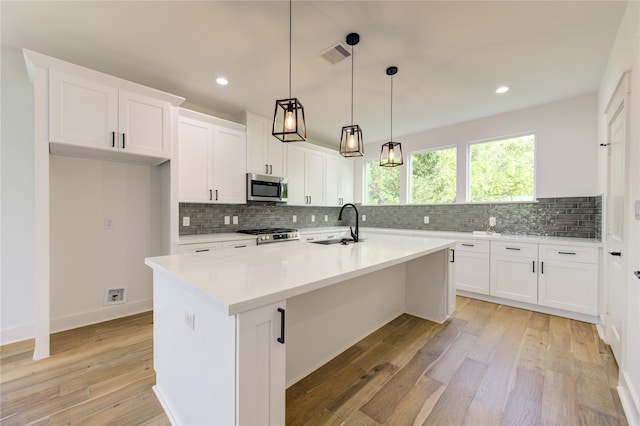 kitchen with visible vents, light wood-style flooring, light countertops, white cabinetry, and stainless steel microwave