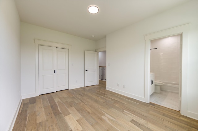 unfurnished bedroom featuring ensuite bathroom, baseboards, light wood-type flooring, and a closet