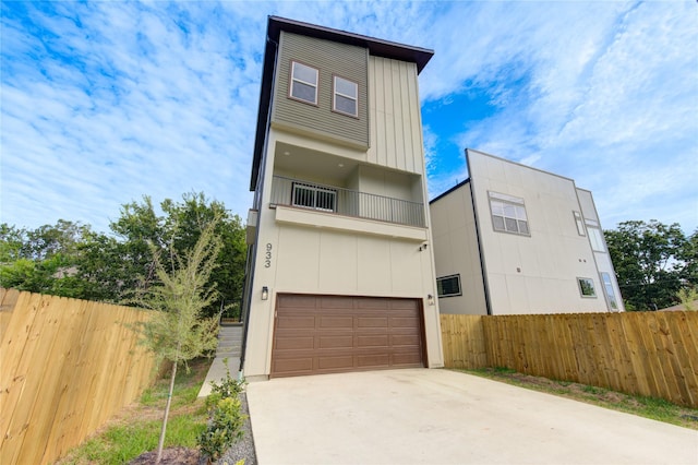 modern home featuring an attached garage, a balcony, driveway, and fence