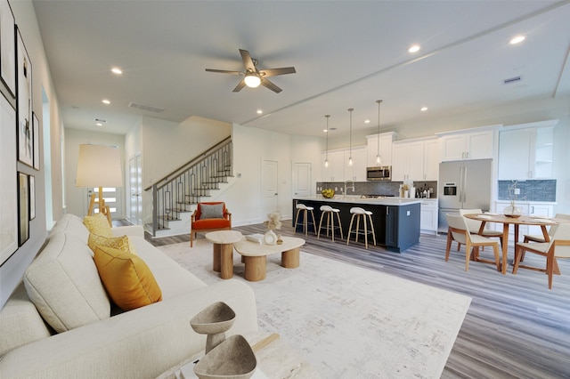 living area with light wood finished floors, visible vents, a ceiling fan, stairway, and recessed lighting