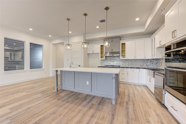 kitchen featuring stainless steel appliances, white cabinetry, a center island with sink, and hanging light fixtures