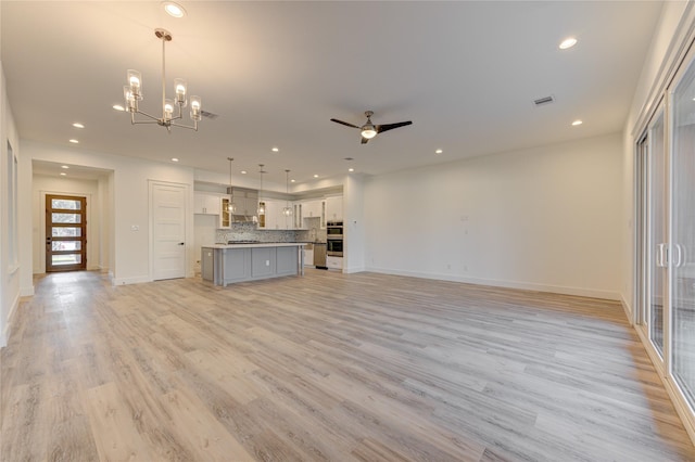 unfurnished living room with recessed lighting, ceiling fan with notable chandelier, visible vents, baseboards, and light wood-style floors