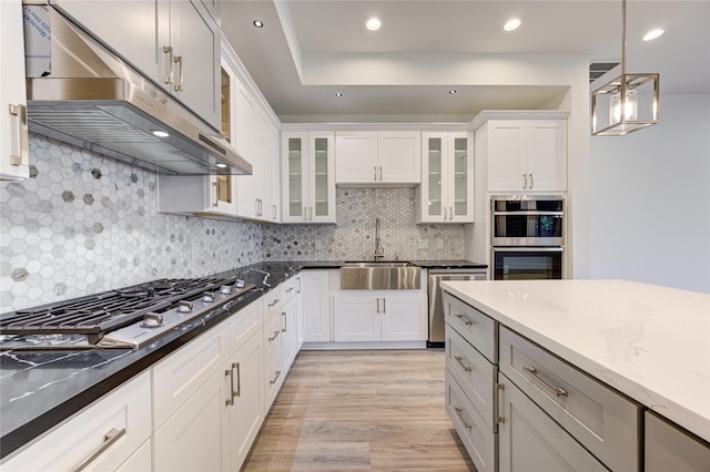 kitchen with decorative light fixtures, stainless steel appliances, ventilation hood, dark stone countertops, and glass insert cabinets